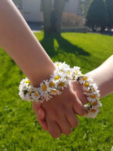 Två händer som håller i varandra med blommor runt handlederna.